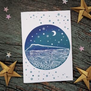 Isle of Portland themed Christmas card featuring the silhouette of the island under a snowy, starry night sky with Chesil beach and the sea in the foreground.
